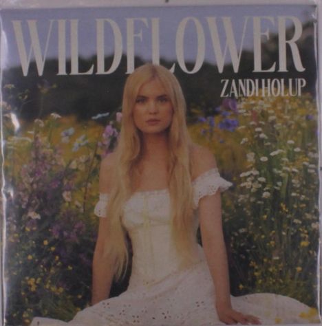 "WILDFLOWER" und "ZANDI HOLUP" in großen Buchstaben; eine Frau in weißem Kleid sitzt in einer blühenden Wiese.