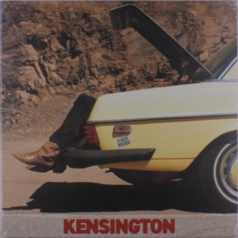 "Kensington" in roter Schrift. Ein gelbes Auto mit geöffneter Kofferraumklappe, Beine mit Cowboy-Stiefeln ragen heraus.