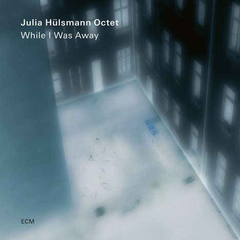 Text: "Julia Hülsmann Octet While I Was Away." Eine verschwommene Ansicht eines Innenhofs mit beleuchteten Fenstern.