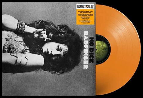 „No Dice, Badfinger“ steht vertikal. Eine Frau mit langen Haaren und Schmuck, daneben eine orangefarbene Vinyl-Schallplatte.