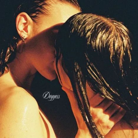 Text: "Deyyess". Zwei Personen küssen sich leidenschaftlich. Licht betont die nassen Haare und Haut der Personen.