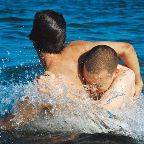 Zwei Personen umarmen sich spielerisch im Wasser, umgeben von spritzenden Wellen.