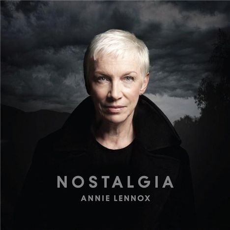 "NOSTALGIA" und "ANNIE LENNOX" vor dunklem, wolkigem Himmel, weißhaarige Person im schwarzen Mantel.