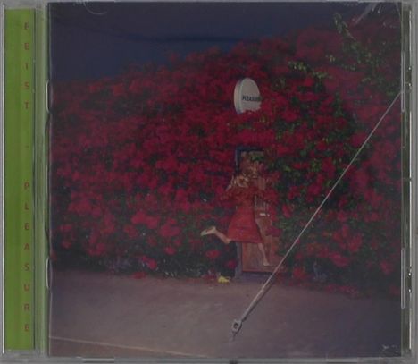 Text: „PLEASURE“, „FEIST“. Eine Frau in Rot steht vor einer Wand aus roten Blumen.