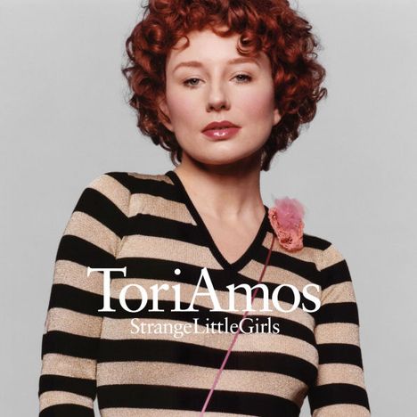"Tori Amos, Strange Little Girls" in weißer Schrift. Person mit rotbraunem Haar, gestreiftem Oberteil und einer Blüte an der Schulter.