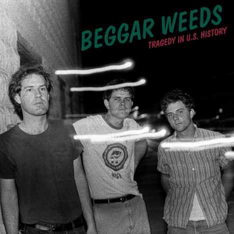"Beggars Weeds. Tragedy in U.S. History." Drei Männer stehen vor einer Wand im Schwarz-Weiß-Foto. Lichtstreifen im Vordergrund.