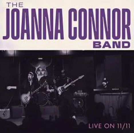 Text: "THE JOANNA CONNOR BAND" und "LIVE ON 11/11". Eine Band spielt auf einer Bühne mit Instrumenten.
