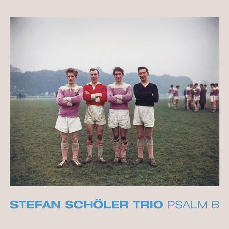 STEFAN SCHÖLER TRIO PSALM B; vier Männer in Fußballkleidung, Arme verschränkt, Gruppe unscharf im Hintergrund, grüne Wiese.