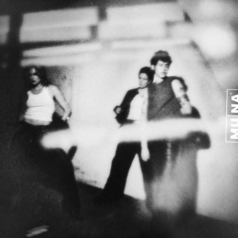 Text "MUNA" erscheint am rechten Rand. Drei unscharfe Personen lehnen an einer Wand, ein Gefühl von Bewegung und Schatten.