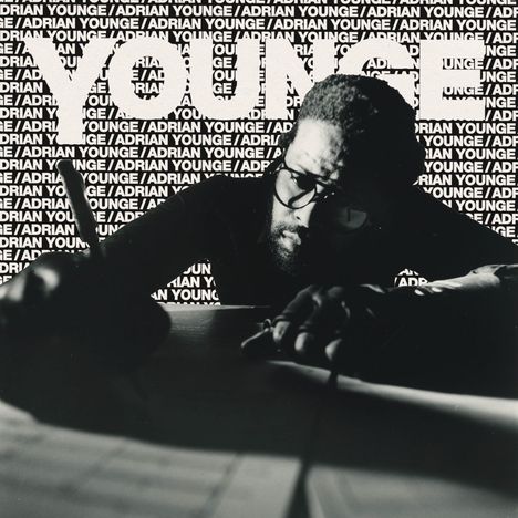 Der Text „ADRIAN YOUNGE“ wiederholt sich oft. Im Vordergrund schreibt ein Mann mit Brille und Bart an einem Tisch.
