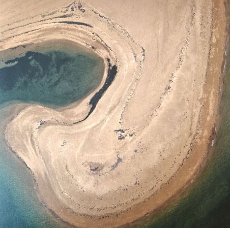 Eine Luftaufnahme zeigt eine spiralförmige Halbinsel mit sandigen, erdigen Tönen und einem grünlichen Wasserbereich.