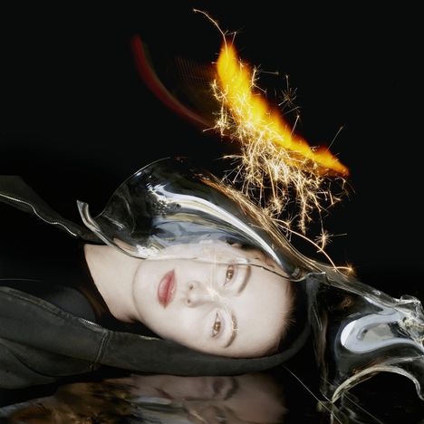 Es gibt keinen Text zu beschreiben. Das Bild zeigt ein Gesicht neben einer gläsernen Skulptur und funkelnden Lichtern.