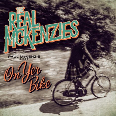Texte: "The Real McKenzies", "Paul McKenzie sings", "On Yer Bike". Ein Mann im Schottenrock fährt mit einem Fahrrad.
