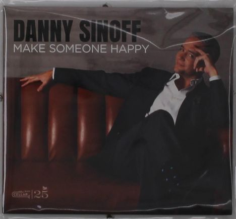 Text: "DANNY SINOFF MAKE SOMEONE HAPPY". Ein Mann im Anzug sitzt entspannt auf einem braunen Ledersofa.