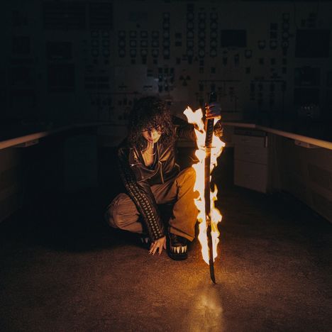 Ich sehe keine lesbaren Texte. Eine Person kniet in einem dunklen Raum und hält ein brennendes Schwert.