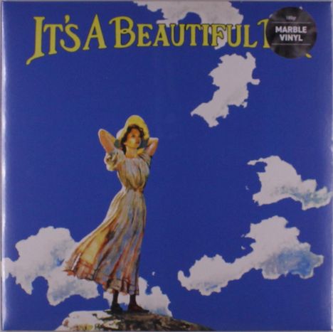 Text: "IT'S A BEAUTIFUL". Auf einem Hügel stehende Frau mit Hut, umgeben von blauem Himmel und weißen Wolken.