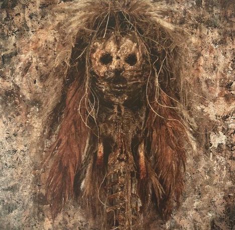 Keine erkennbaren Texte. Eine düstere, skulpturähnliche Figur mit Federn und maskenartigem Gesicht vor bräunlichem Hintergrund.
