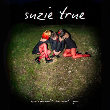 Der Text lautet "suzie true" und "how i learned to love what’s gone". Drei Personen sitzen umarmt auf grasigem Boden.