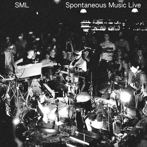 Text oben: „SML Spontaneous Music Live“. Schwarz-Weiß-Aufnahme einer Band, die vor Publikum spielt.
