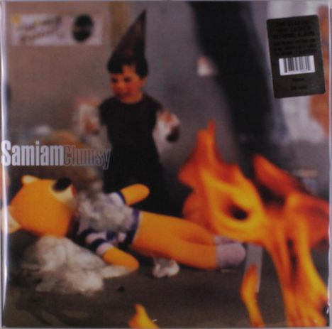 "Samiam Clumsy" Text mit verschwommenem Hintergrund: Kind mit Partyhut, Stofftier und Flammen im Vordergrund.