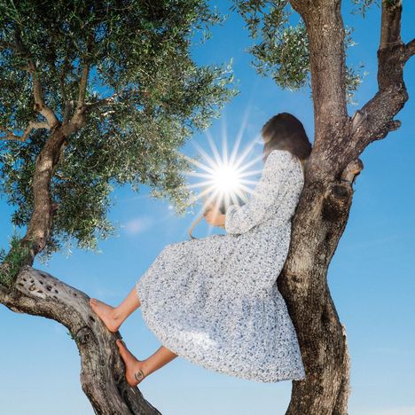 Keine Texte sichtbar. Eine Frau sitzt barfuß auf einem Baum und hält einen hellen Lichtstrahl.