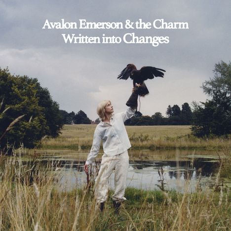 „Avalon Emerson & the Charm, Written into Changes“. Eine Person in weißer Kleidung hält einen Greifvogel auf einer Wiese.