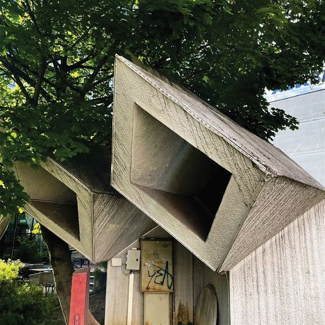 Ein Kasten ist mit "y2b" beschriftet. Große, geometrische Lüftungsschächte ragen zwischen Bäumen hervor.