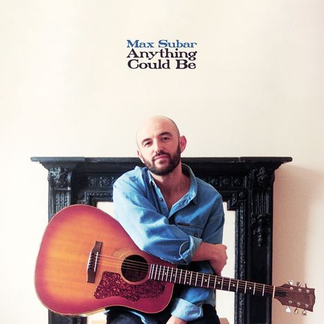 Text: "Max Subar Anything Could Be". Ein Mann mit Glatze, Bart und Gitarre, sitzt vor einem schwarzen Kamin und trägt ein blaues Hemd.