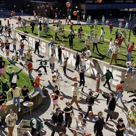 Auf einer Betonwand steht "NEELS", umgeben von vielen Menschen, die Basketball spielen und Musikinstrumente halten.