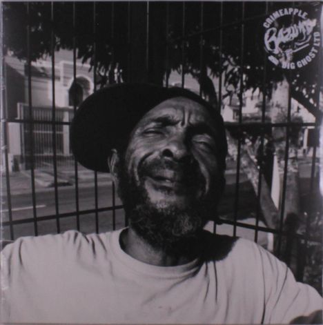 Text oben: "CRIMEAPPLE x BIG GHOST LTD". Ein lächelnder Mann mit schiefem Hut, hinter Gitterzaun sitzend, in Schwarzweiß.