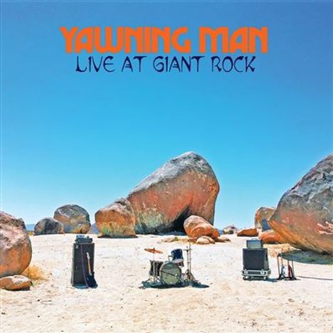 „YAWNING MAN LIVE AT GIANT ROCK“ in Blau und Orange. Wüstenlandschaft mit Musikinstrumenten und großen Felsen.