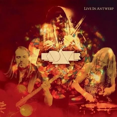 Text: "LIVE IN ANTWERP". Im Hintergrund spielen drei Musiker leidenschaftlich auf der Bühne. Psychedelische Farben.