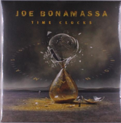 "JOE BONAMASSA TIME CLOCKS." Eine kaputte Sanduhr in einer kargen Landschaft, mit verstreutem Sand und Scherben.