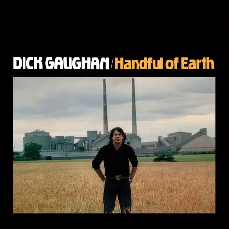 "DICK GAUGHAN / Handful of Earth." Ein Mann steht auf einem Feld vor einer Industrieanlage mit zwei Schornsteinen.