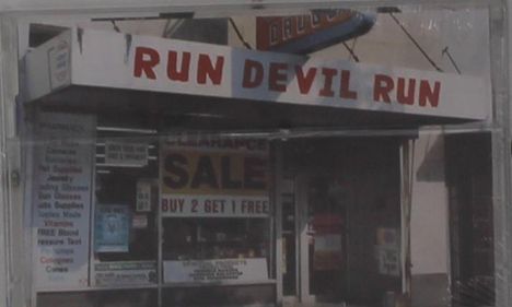"RUN DEVIL RUN" ist in Rot auf einem Ladenschild zu sehen. Darunter ein Schild: "CLEARANCE SALE BUY 2 GET 1 FREE".