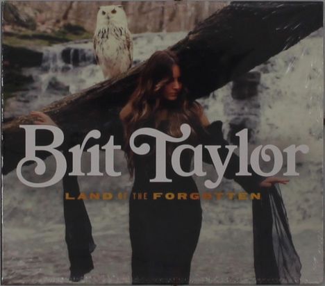"Brit Taylor" und "LAND OF THE FORGOTTEN" Text. Eine Frau in Schwarz, eine Eule sitzt auf einem Ast im Wald.