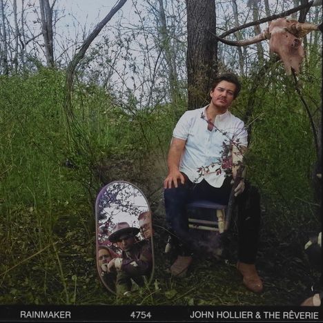 Text: "RAINMAKER 4754 JOHN HOLLIER & THE RÉVERIE". Ein Mann sitzt im Wald, neben einem Spiegel mit reflektierten Gesichtern.