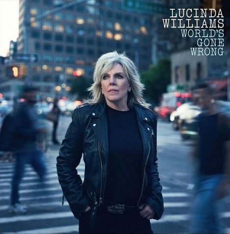 Text: "Lucinda Williams World's Gone Wrong". Frau in schwarzer Lederjacke steht auf einer belebten Straße in der Stadt.