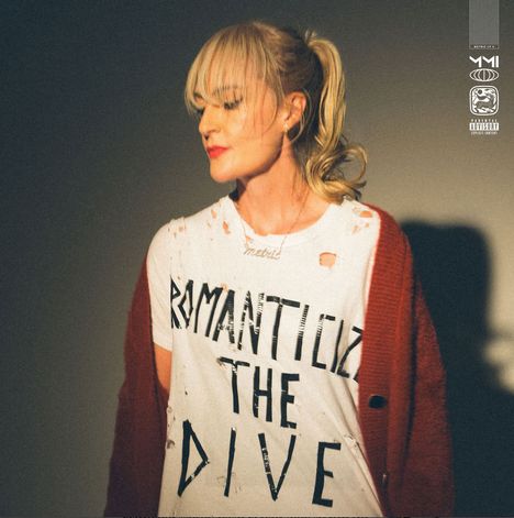 Auf dem zerrissenen T-Shirt steht "ROMANTICIZE THE DIVE". Eine Frau mit blondem Pferdeschwanz trägt es, dazu eine rote Jacke.
