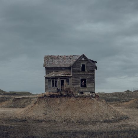 Holzhaus auf Erdhügel, verlassenes Aussehen, grauer Himmel, einsame Lage, verwittert und unbewohnt.