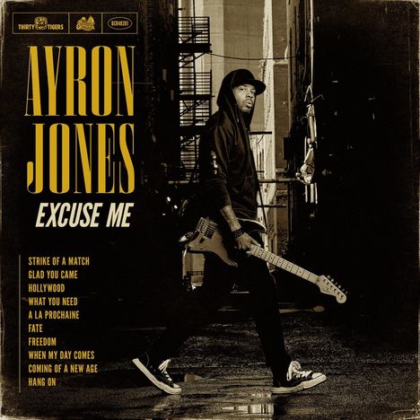 Große Schrift: AYRON JONES. Weitere Texte: EXCUSE ME, Strike of a Match, Glad You Came. Person mit Gitarre in einer Gasse.