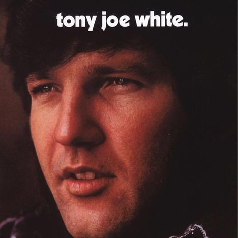 Text: "tony joe white." Nahaufnahme eines Mannes mit dunklen Haaren und ernstem Blick, Gesicht leicht zur Seite gedreht.