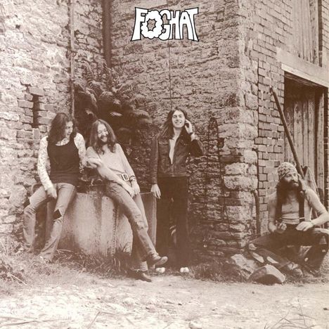 "FOGHAT" steht oben. Vier Männer lehnen entspannt an einer alten Steinmauer, einer sitzt mit Mütze. Retro-Stil.