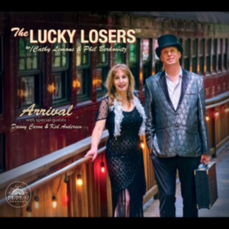 "The Lucky Losers. Arrival. Mit Cathy Lemons & Phil Berkowitz. Danny Caron & Kid Andersen. Zwei Personen neben einem Zug."