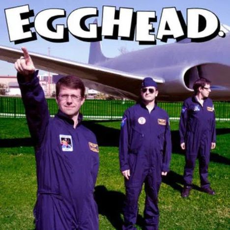 "EGGHEAD." Text oben, darunter drei Männer in blauen Overalls vor einem Flugzeug auf einer Wiese.