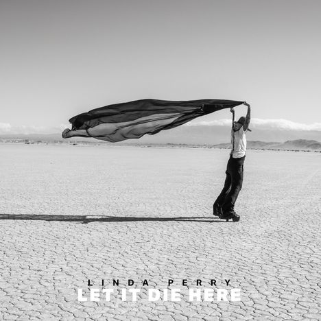 Text: "LINDA PERRY LET IT DIE HERE". Eine Person in der Wüste hält ein großes Tuch im Wind über dem Kopf.