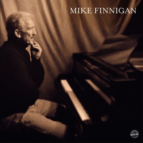 Text: "MIKE FINNIGAN." Ein Mann sitzt am Klavier, den Kopf nachdenklich auf seine Hand gestützt.