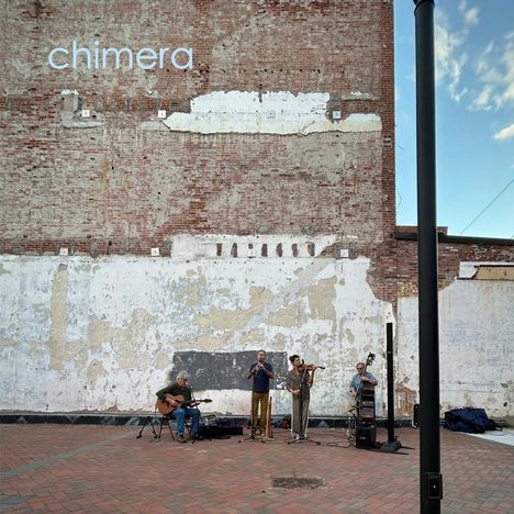 Der Text "chimera" steht groß an einer verputzten Backsteinwand, davor spielt eine vierköpfige Band auf einer gepflasterten Fläche.