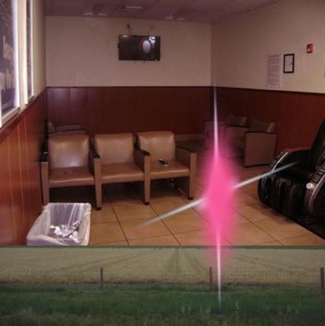 An der Wand hängt ein Fernseher. Ein Wartezimmer mit braunen Stühlen, einer großen schwarzen Liege und einem Mülleimer.