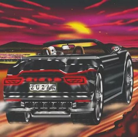 "ZUZAX" auf dem Nummernschild eines schwarzen Cabriolets, das bei Sonnenuntergang über eine staubige Straße fährt.